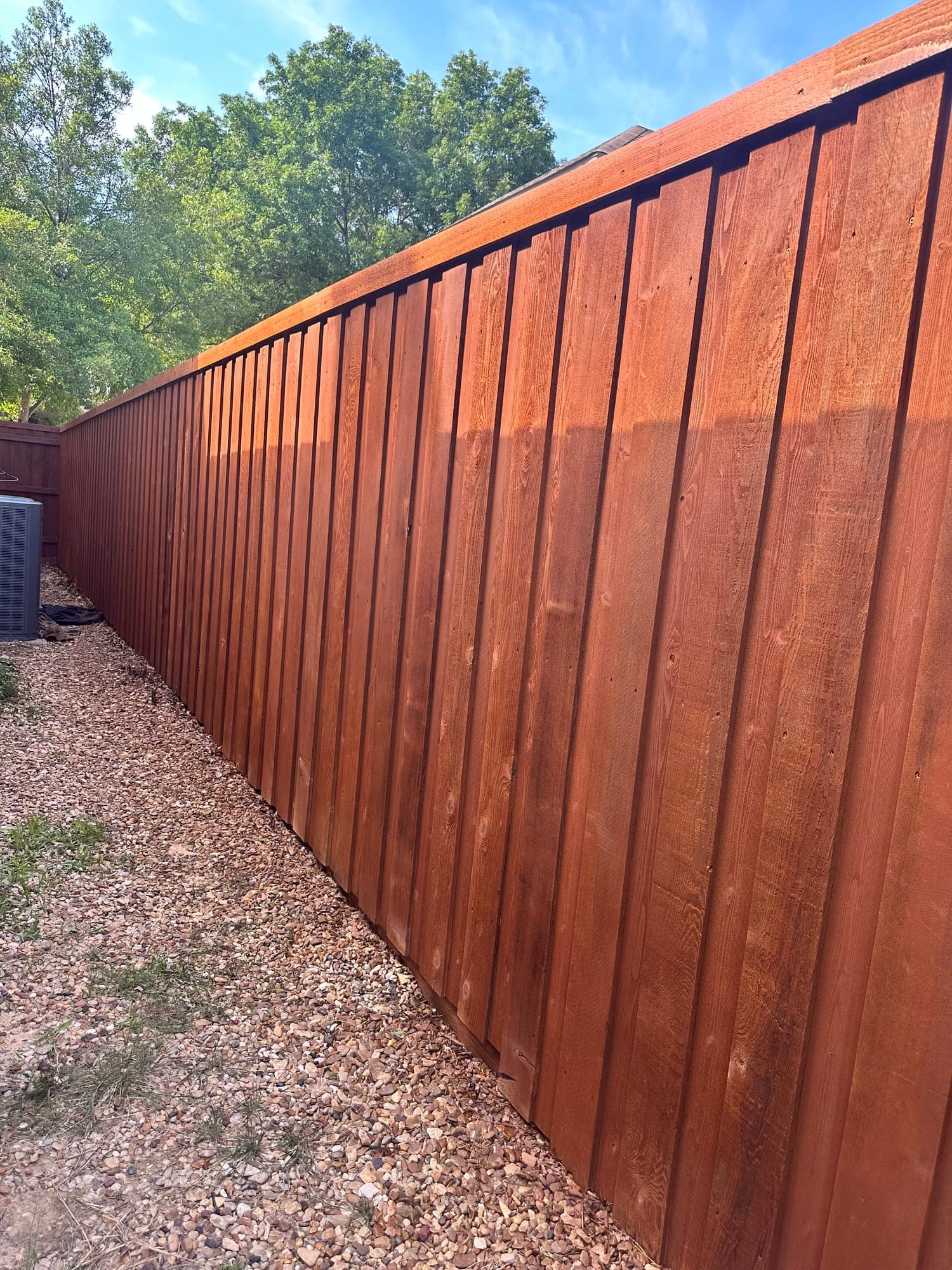 Reddish-brown stained wood fence running along a gravel side yard