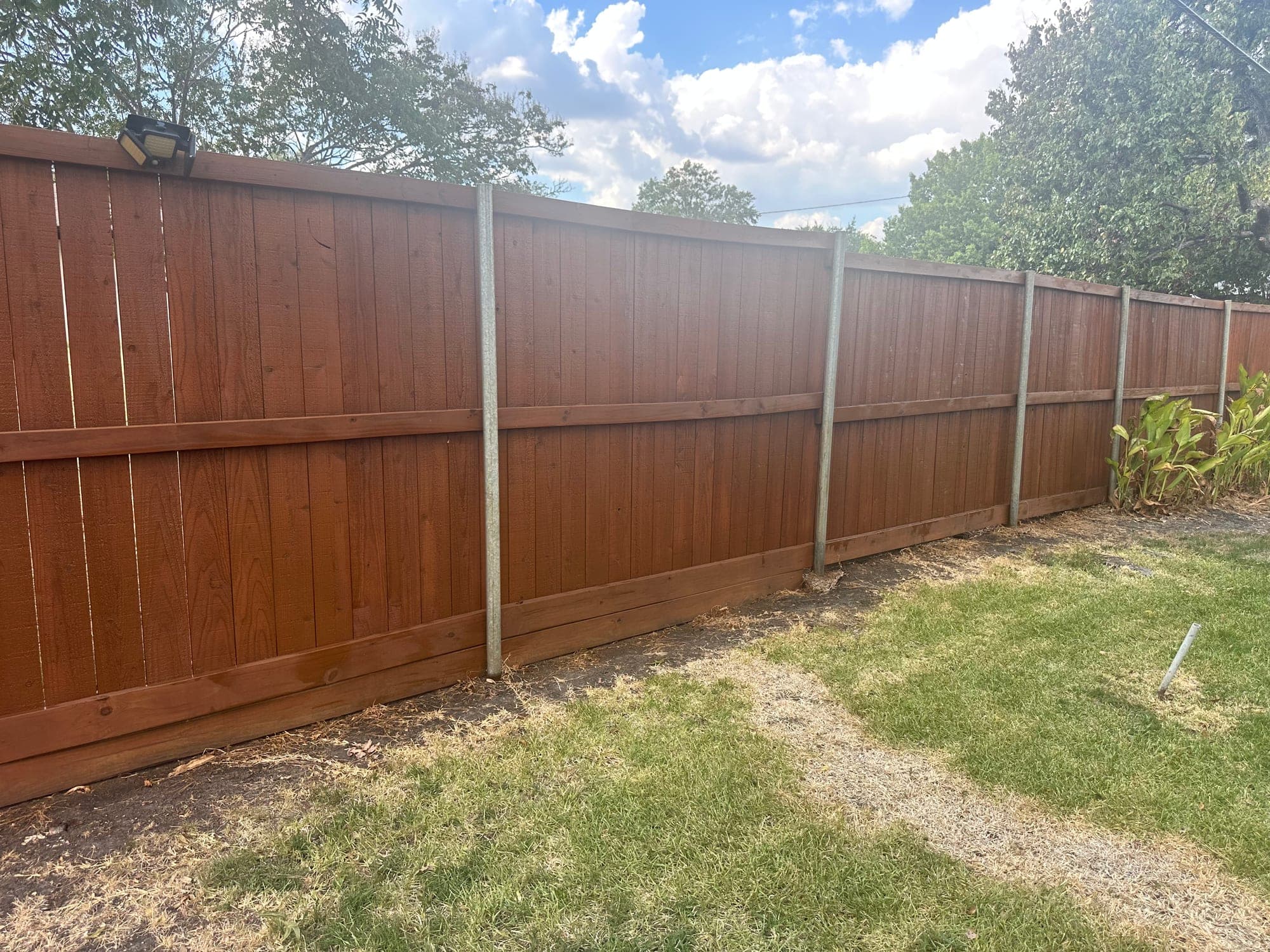 Long stained wood privacy fence with horizontal rails and galvanized metal posts beside a backyard lawn